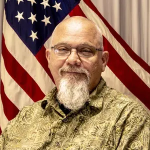 A man with a beard and glasses in front of an american flag.