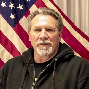 A man in black hoodie standing next to an american flag.